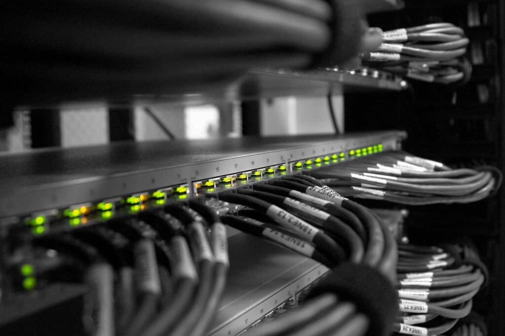 Rack réseau comportant une rangée de LED vertes allumées sur un commutateur et des câbles Ethernet regroupés, étiquetés et rangés dans une armoire serveur