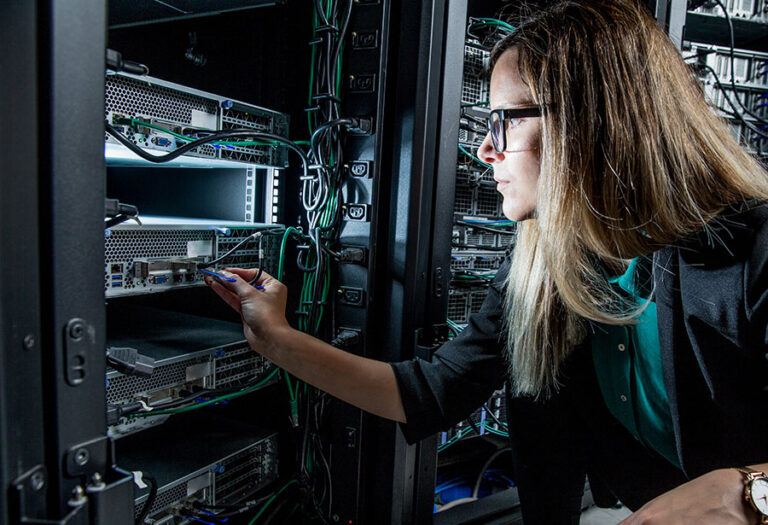 Weibliche IT-Technikerin in einem Rechenzentrum steckt ein Netzwerkabel in einen Rack-Server.