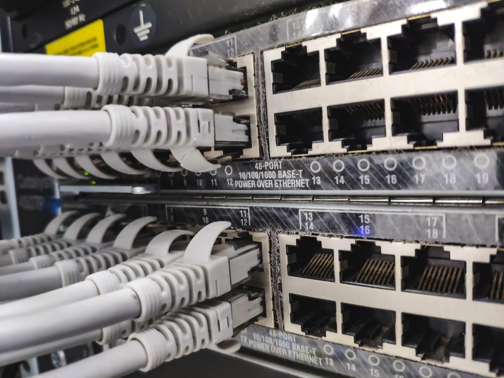 Close-up of a network patch panel with multiple RJ-45 Ethernet ports and gray cables plugged into them in a server rack, showing data cabling.